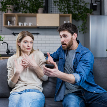 A man animatedly talking to a woman who appears disinterested or uncomfortable, while sitting on a couch.