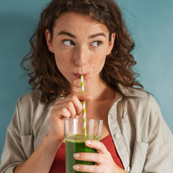 Woman drinking a green smoothie through a straw.