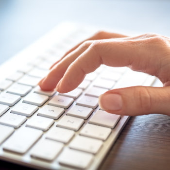 A person's hand typing on a white computer keyboard.