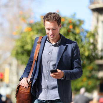 Man walking outdoors while looking at his smartphone.
