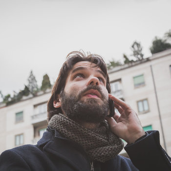 Man with a beard having a phone conversation while looking upward, standing outdoors.