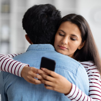 A woman hugging a man while secretly looking at her smartphone.