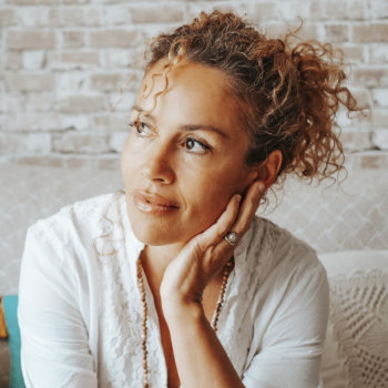 Woman with curly hair lost in thought, resting chin on hand.
