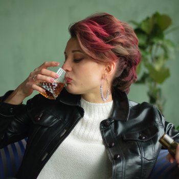 Woman with pink hair drinking from a small bottle.
